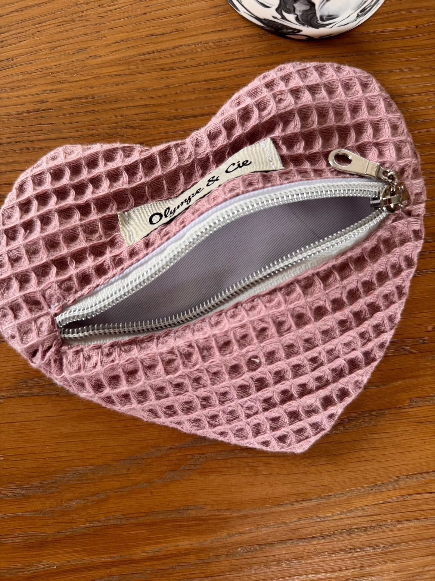 Porte-monnaie rose en forme de cœur avec fermeture éclair et étiquette "Olympe & Cie".