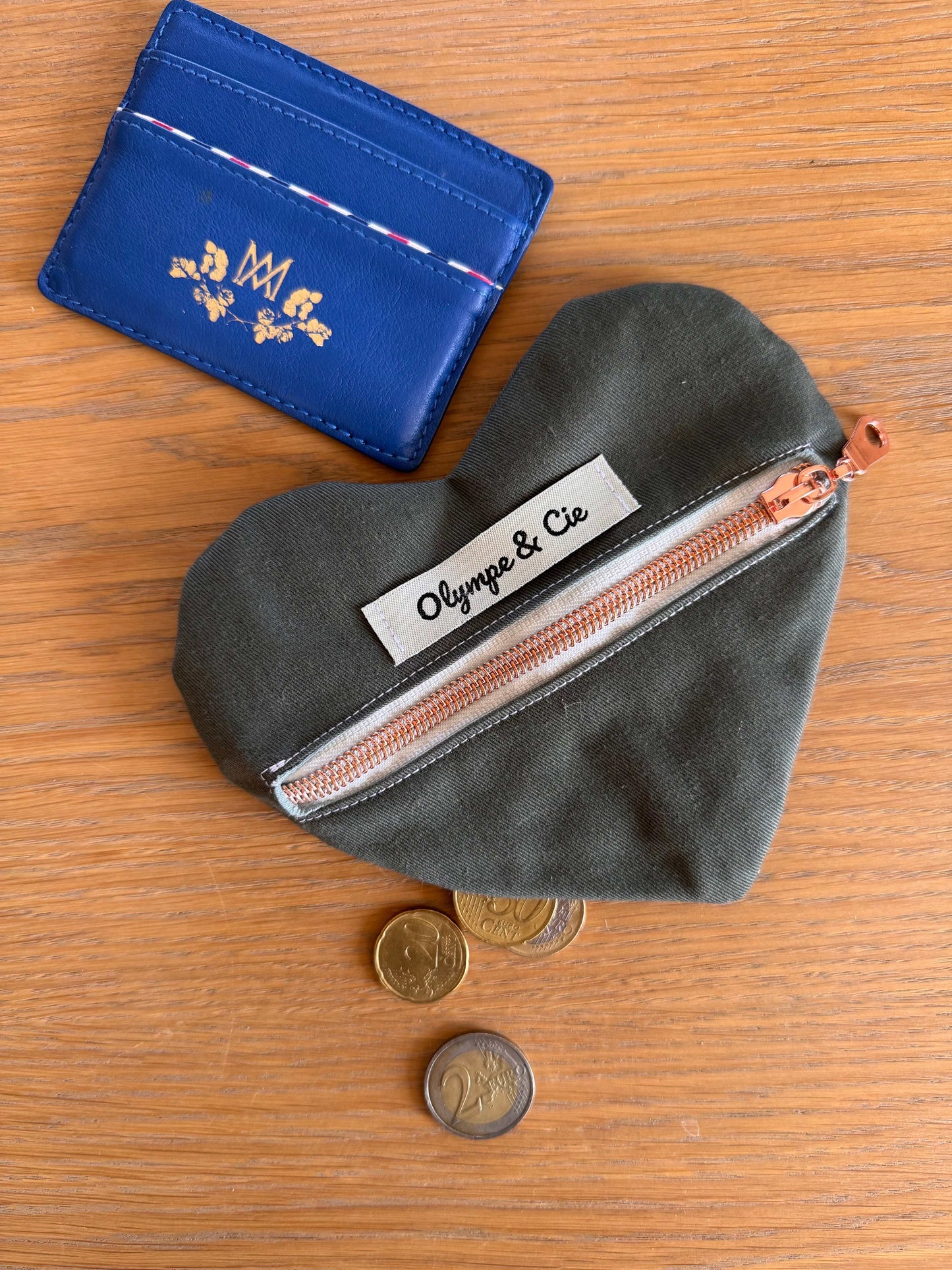 Porte-monnaie kaki en forme de cœur avec fermeture éclair et étiquette "Olympe & Cie".